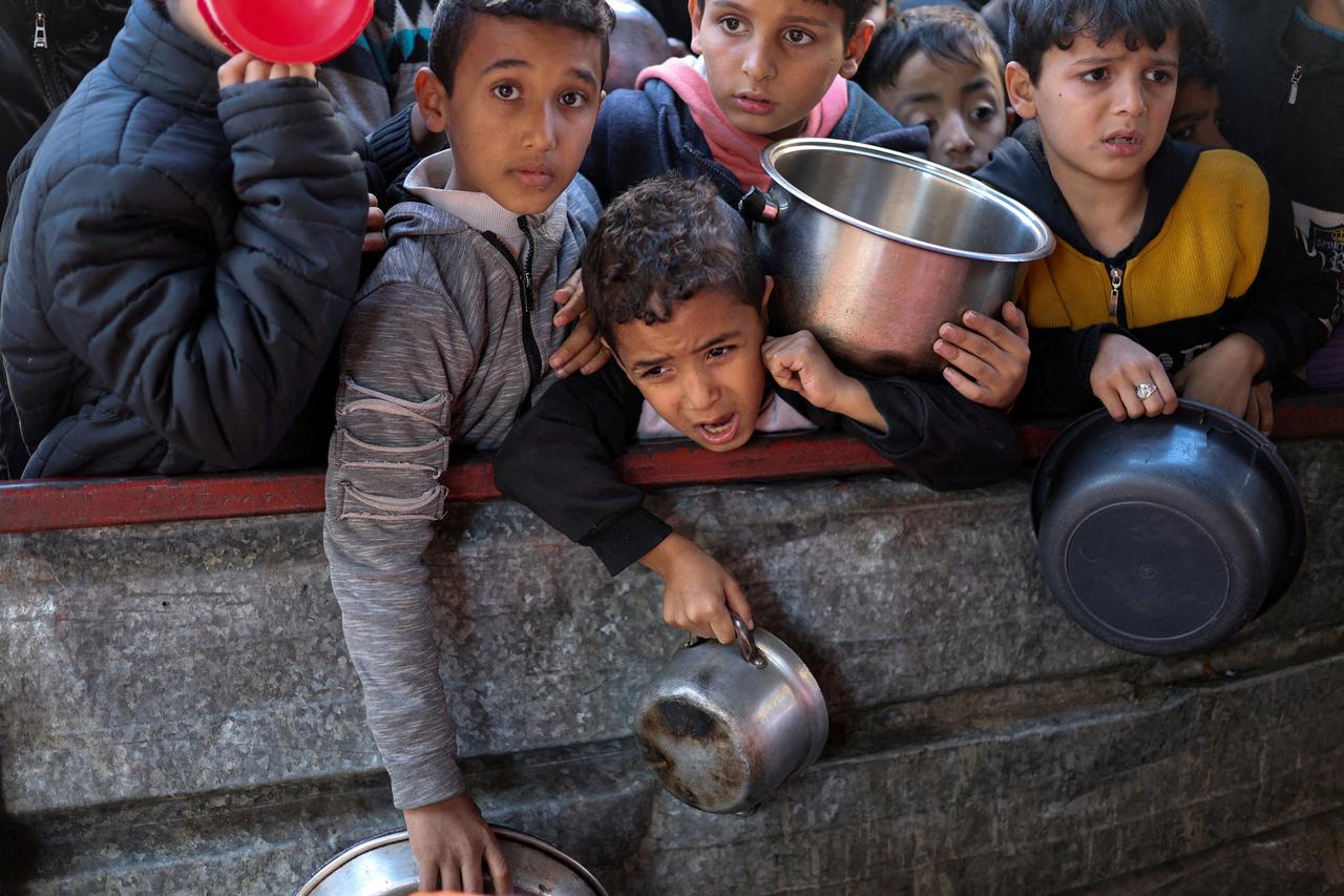FILE PHOTO: Palestinians wait to receive food cooked by a charity kitchen amid shortages, in Rafah