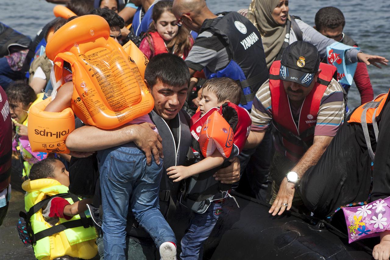 A Syrian refugee (L) carries two children after arriving on a dinghy on the Greek island of Lesbos, September 7, 2015. Greece is struggling to cope with the hundreds of migrants and refugees from the war in Syria making the short crossing every day from T