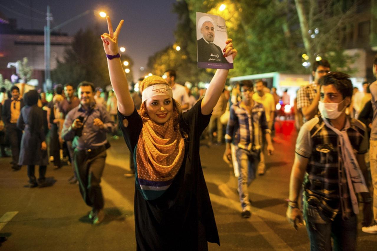 'A supporter of moderate cleric Hassan Rohani gestures with a picture of him as she celebrates his victory in Iran\'s presidential election on a street in Tehran June 15, 2013. Rohani won Iran\'s pres