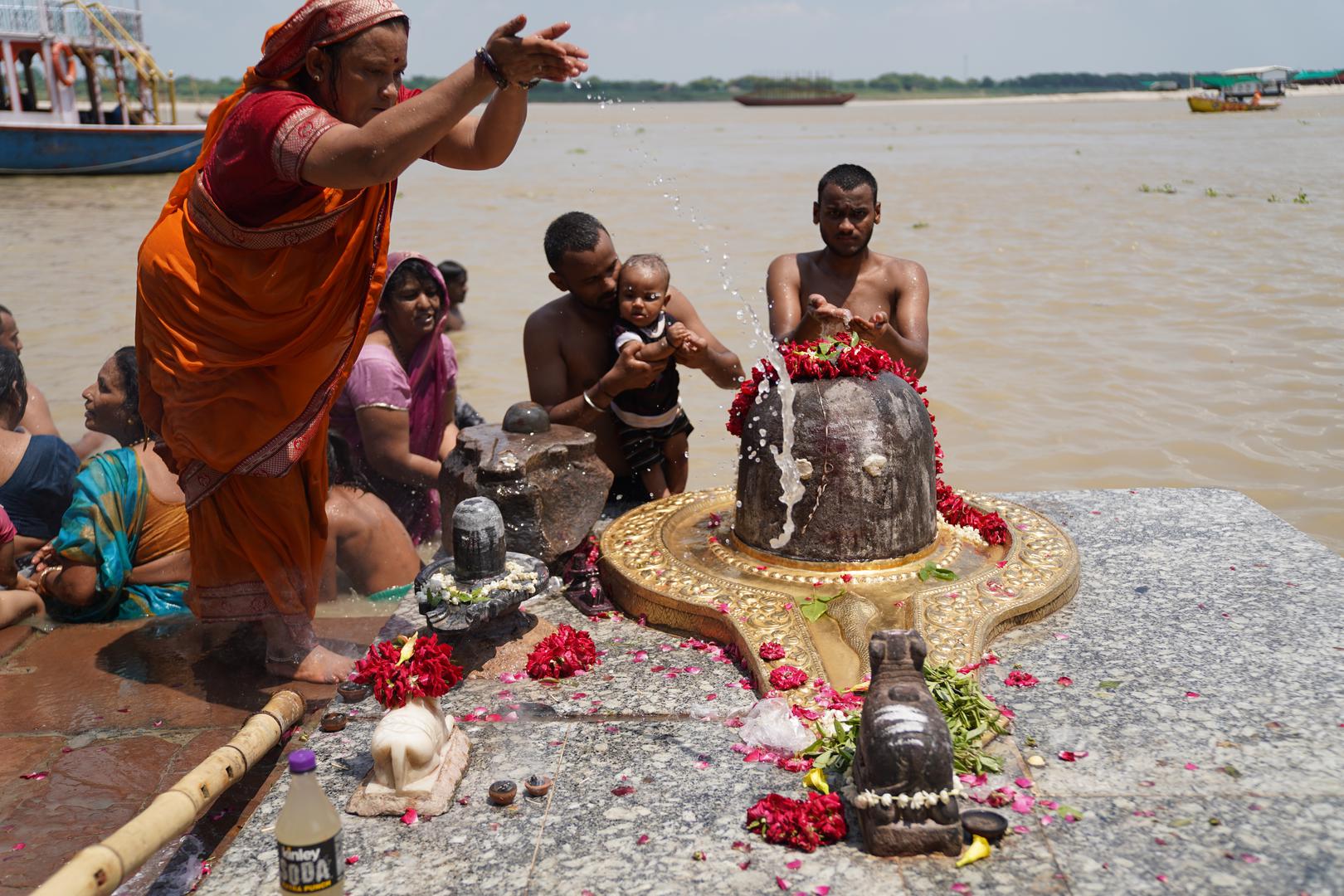 19 July 2024, India, Varanasi: A family prays to a symbol of the god Shiva - among other things by pouring water from the Ganges over it. Beforehand, they have also sunk the ashes of their relatives in the river. Shiva is the most important deity of Varanasi. Photo: Anne-Sophie Galli/dpa Photo: Anne-Sophie Galli/DPA