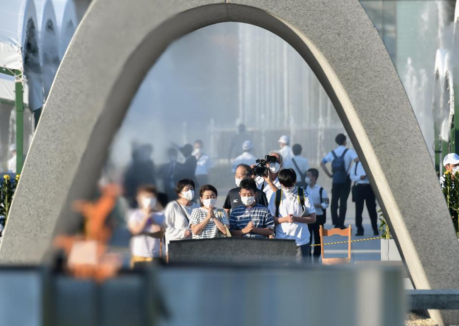 People wearing protective face masks pray in front of the cenotaph for the victims of the 1945 atomic bombing of Hiroshima by the United States