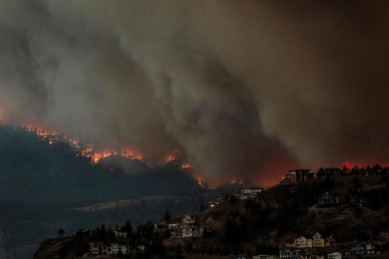 Smoke and flames from wildfires serve as a backdrop for homes across Okanagan Lake in West Kelowna, British Columbia, Canada, August 17, 2023. REUTERS/Dan Riedlhuber Photo: DAN RIEDLHUBER/REUTERS