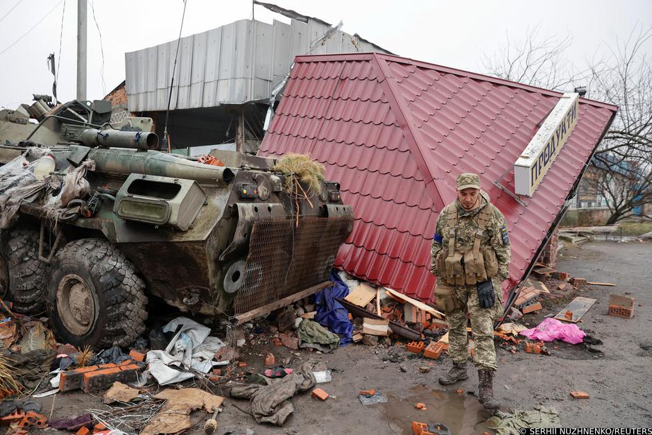 Ukrainian service member walks next to a damaged Russian BTR-82 in the village of Nova Basan