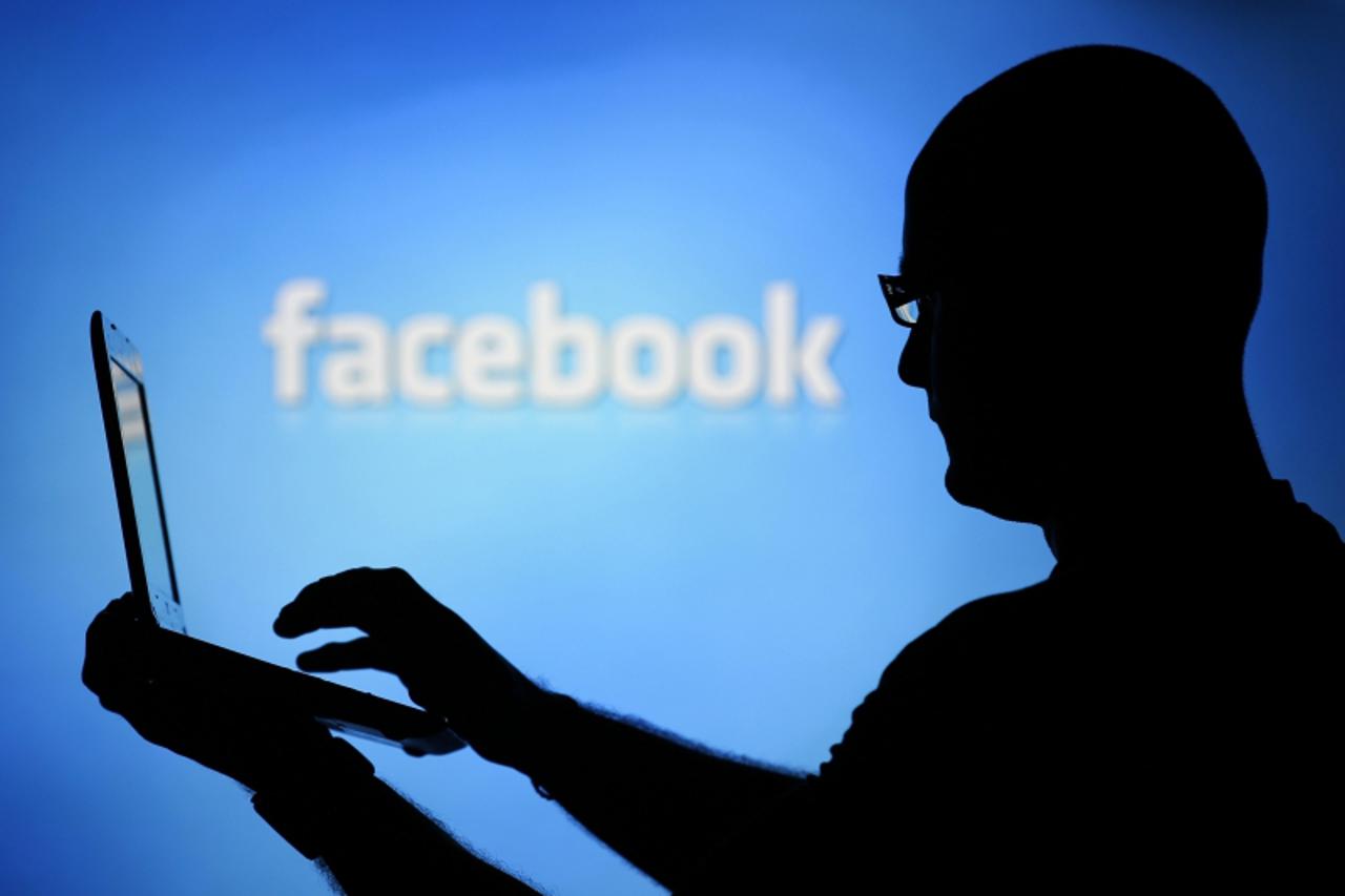 'A man is silhouetted against a video screen with an Facebook logo as he poses with an Dell laptop in this photo illustration taken in the central Bosnian town of Zenica, August 14, 2013. REUTERS/Dado