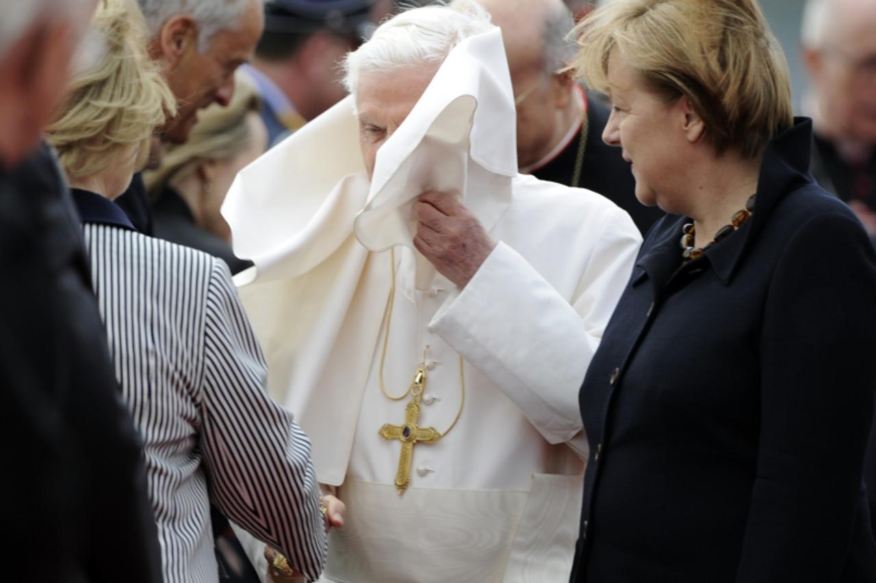 'Pope Benedict XVI (C) has his robe blown in the face by the wind as he is welcomed by German Chancellor Angela Merkel (R) and members of the German cabinet after arriving on September 22, 2011 at the