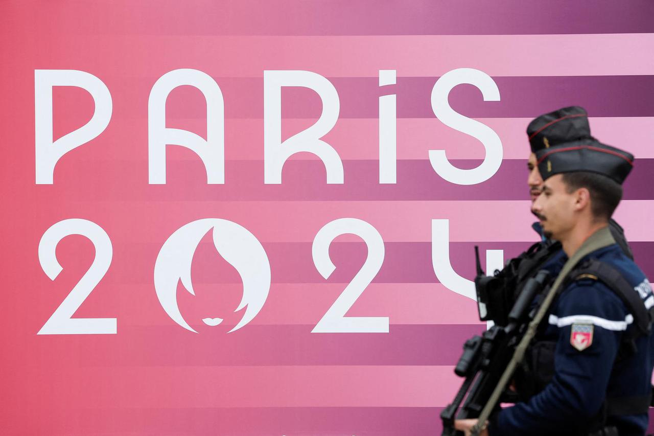 French gendarmes walk past the logo of the Paris 2024 Olympic and Paralympic Games in front of the National Assembly in Paris