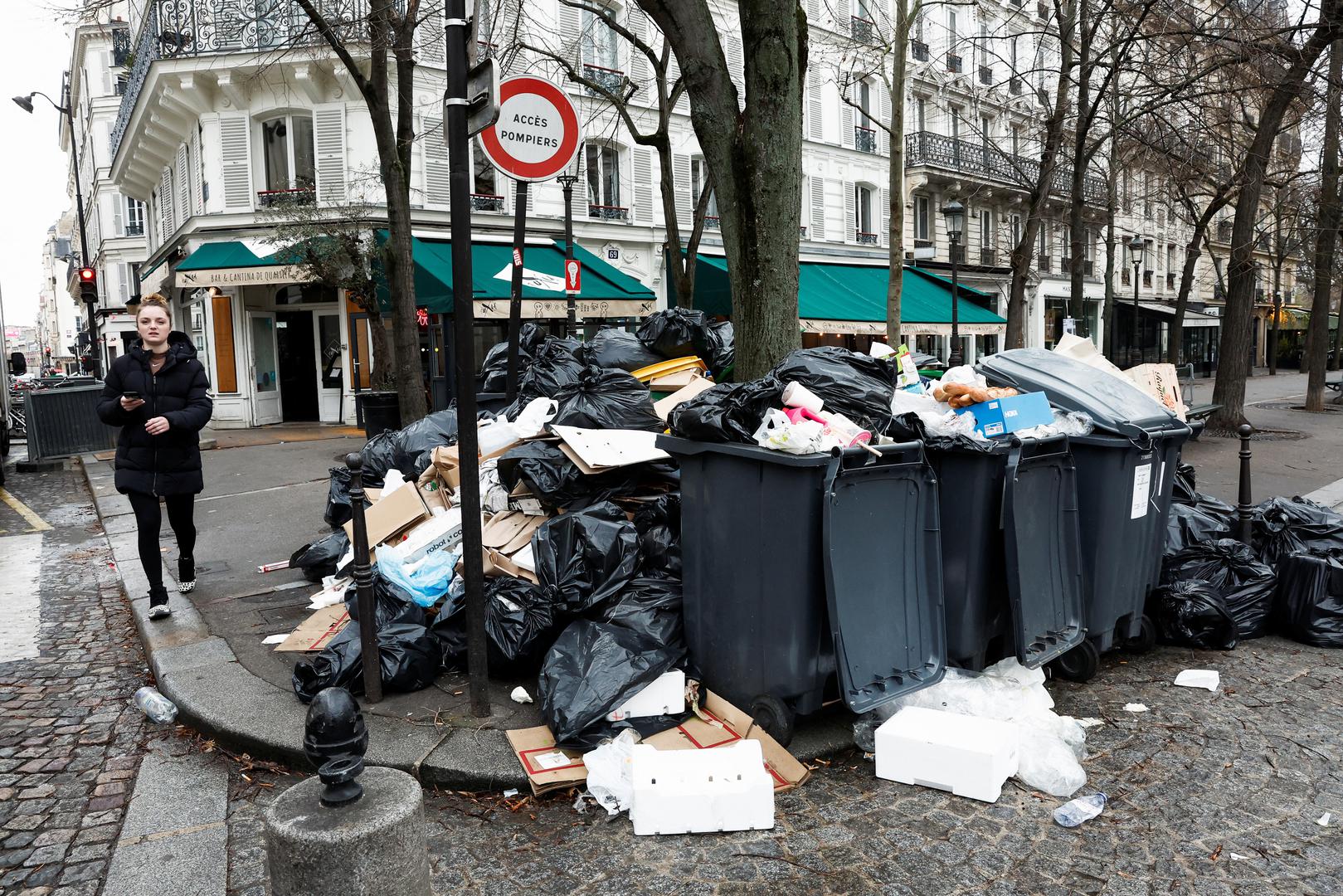 People walk in a street where garbage cans are overflowing, as garbage has not been collected, in Paris, France March 13, 2023. REUTERS/Benoit Tessier Photo: BENOIT TESSIER/REUTERS