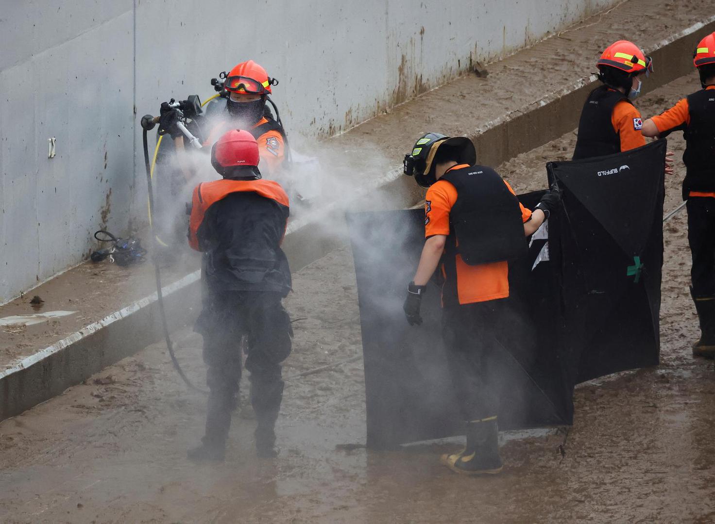 Rescue workers hose themselves down during a search and rescue operation near an underpass that has been submerged by a flooded river caused by torrential rain in Cheongju, South Korea, July 16, 2023.   REUTERS/Kim Hong-ji Photo: KIM HONG-JI/REUTERS