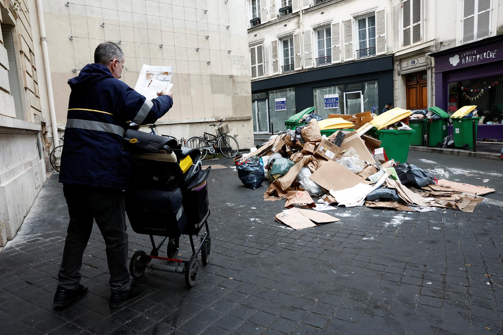 People walk in a street where garbage cans are overflowing, as garbage has not been collected, in Paris, France March 13, 2023. REUTERS/Benoit Tessier Photo: BENOIT TESSIER/REUTERS