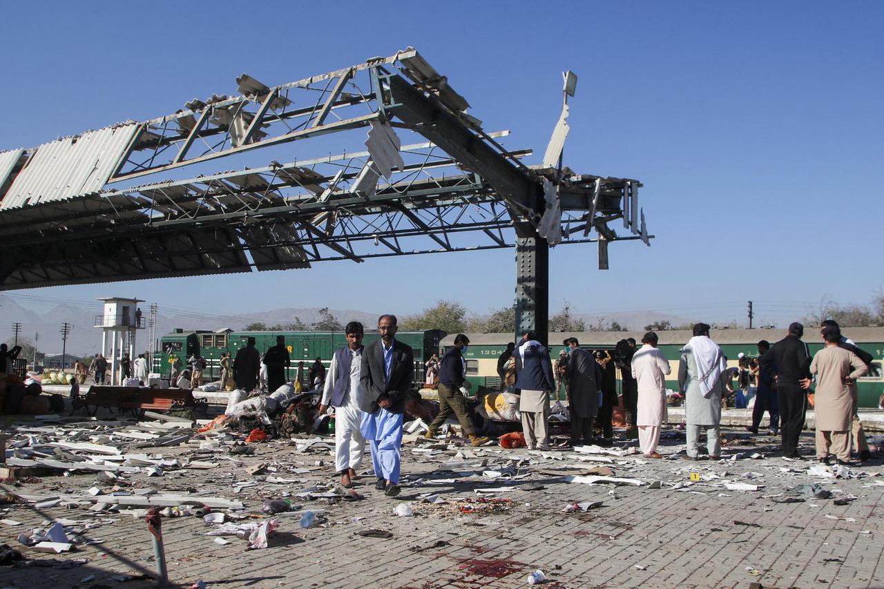 People walk amid debris after a bomb blast at a railway station in Quetta