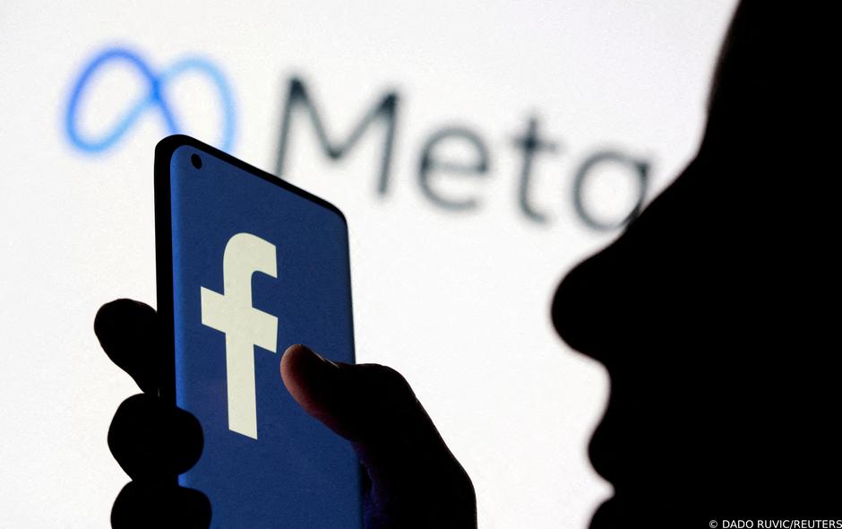 FILE PHOTO: Woman holds smartphone with Facebook logo in front of a displayed Facebook's new rebrand logo Meta in this illustration picture