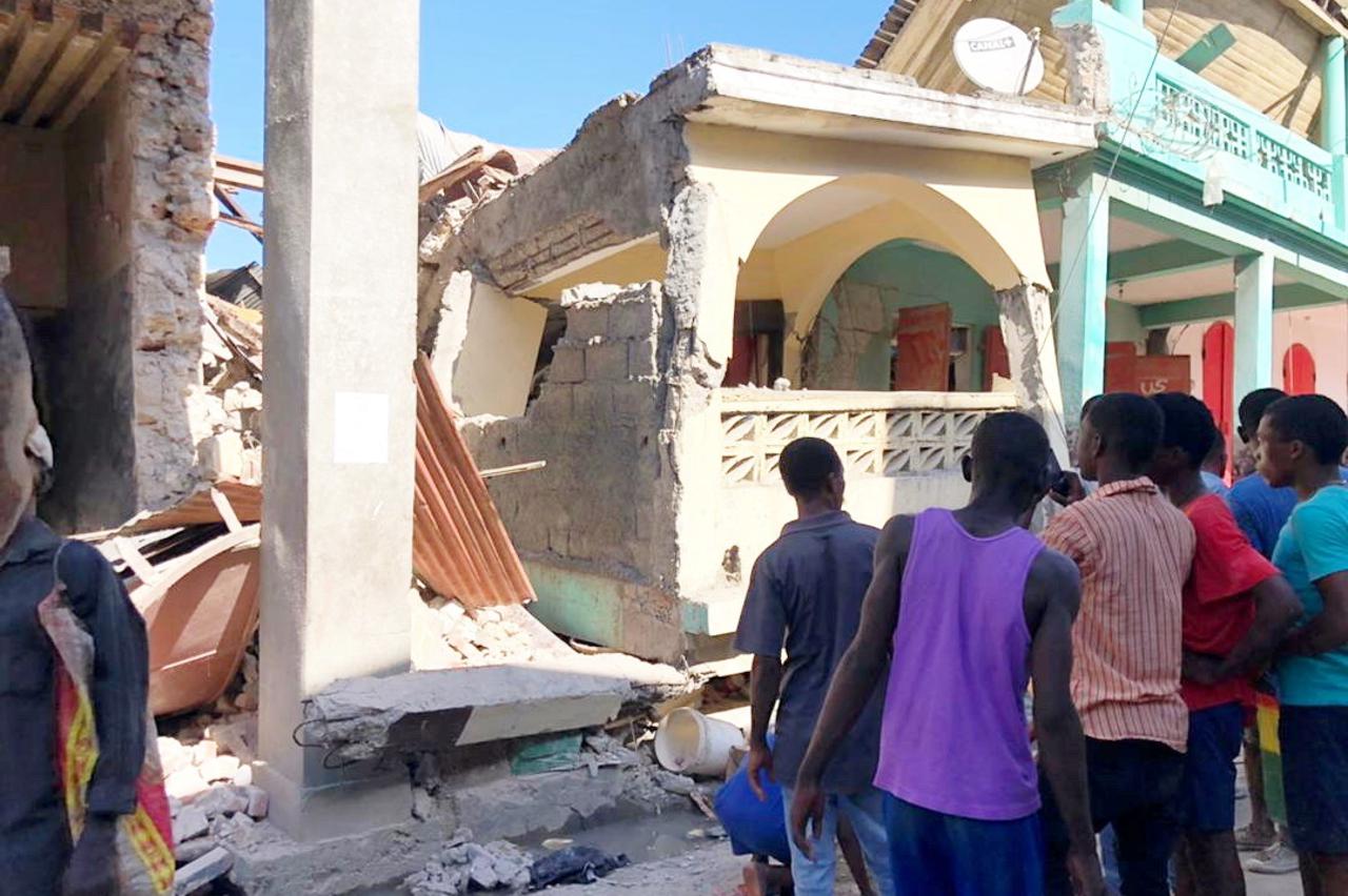 People stand in front of collapsed buildings following an earthquake in Jeremie