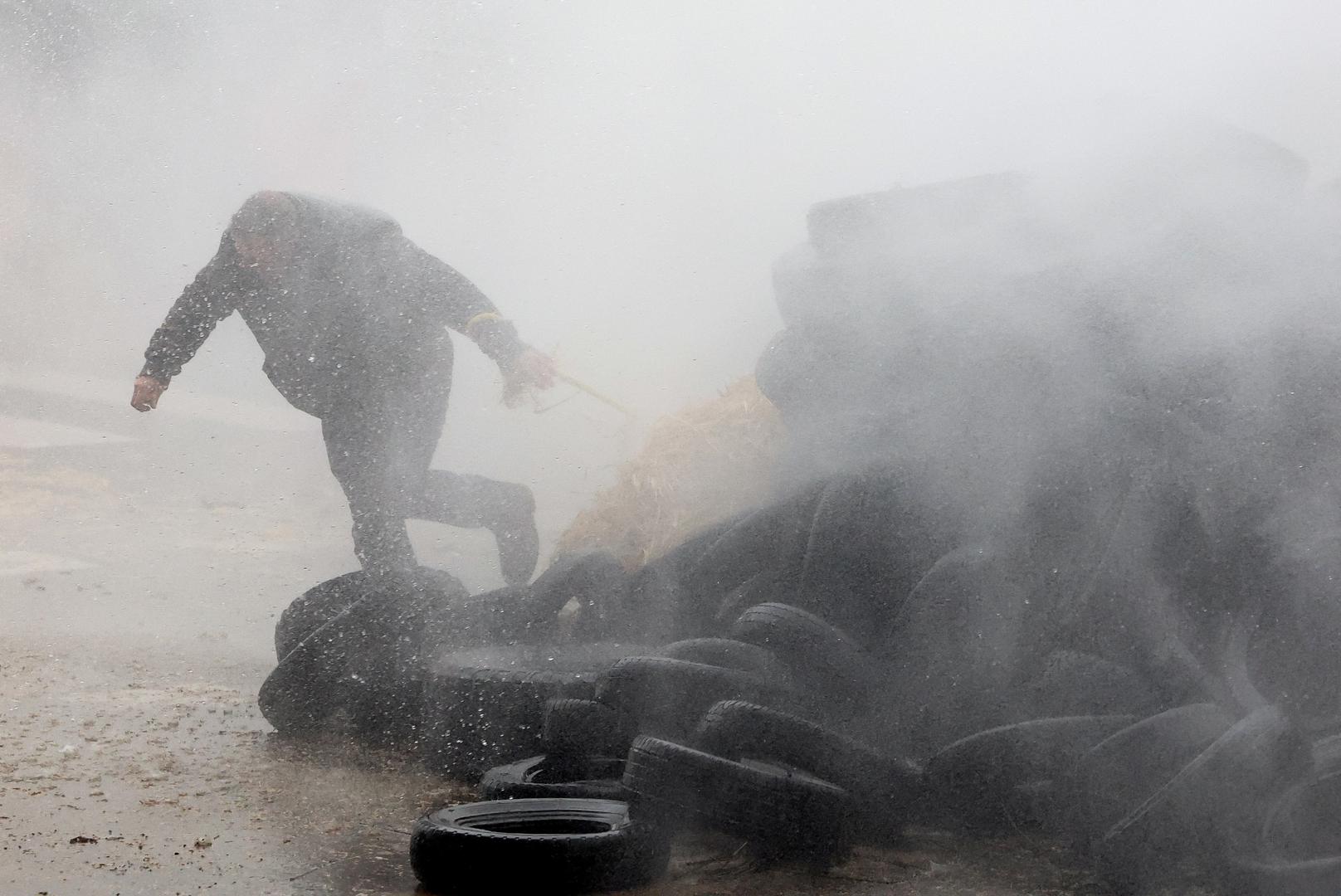 A farmer runs behind tires as he is sprayed by a water cannon during a protest of European farmers over price pressures, taxes and green regulation, on the day of an EU Agriculture Ministers meeting in Brussels, Belgium February 26, 2024. REUTERS/Yves Herman     TPX IMAGES OF THE DAY Photo: YVES HERMAN/REUTERS