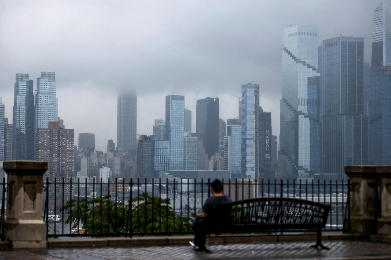 A person looks at the Empire State building and the New York skyline covered in fog during a rainy morning, as seen from Weehawken, New Jersey