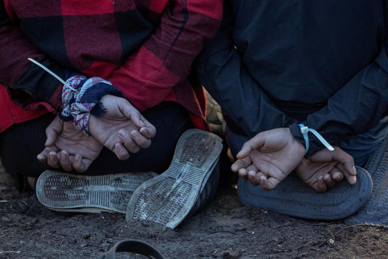 FILE PHOTO: Detained migrants sit on their knees with cuffed hands, at their makeshift camp close to the Serbia-Hungary border