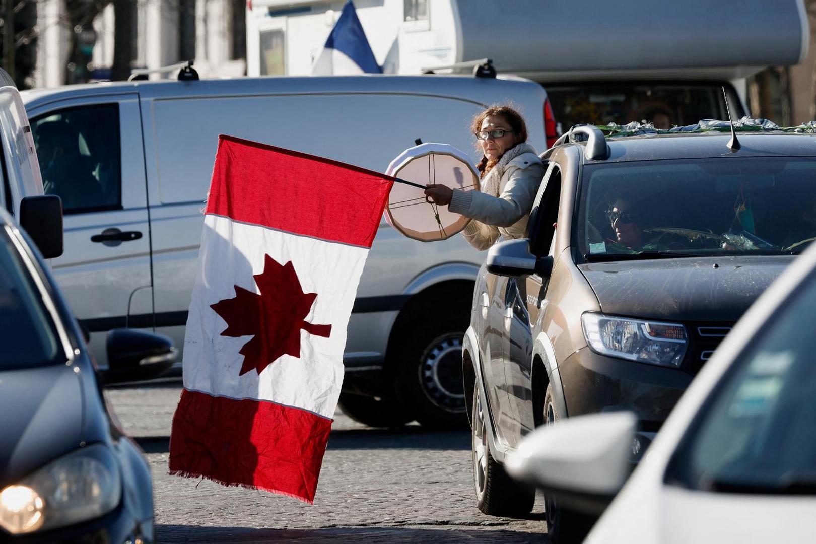 A protester waves a Canadian flag on the Champs-Elysees avenue as cars parade during their "Convoi de la liberte" (The Freedom Convoy), a vehicular convoy to protest coronavirus disease (COVID-19) vaccine and restrictions in Paris, France, February 12, 2022. REUTERS/Benoit Tessier Photo: BENOIT TESSIER/REUTERS