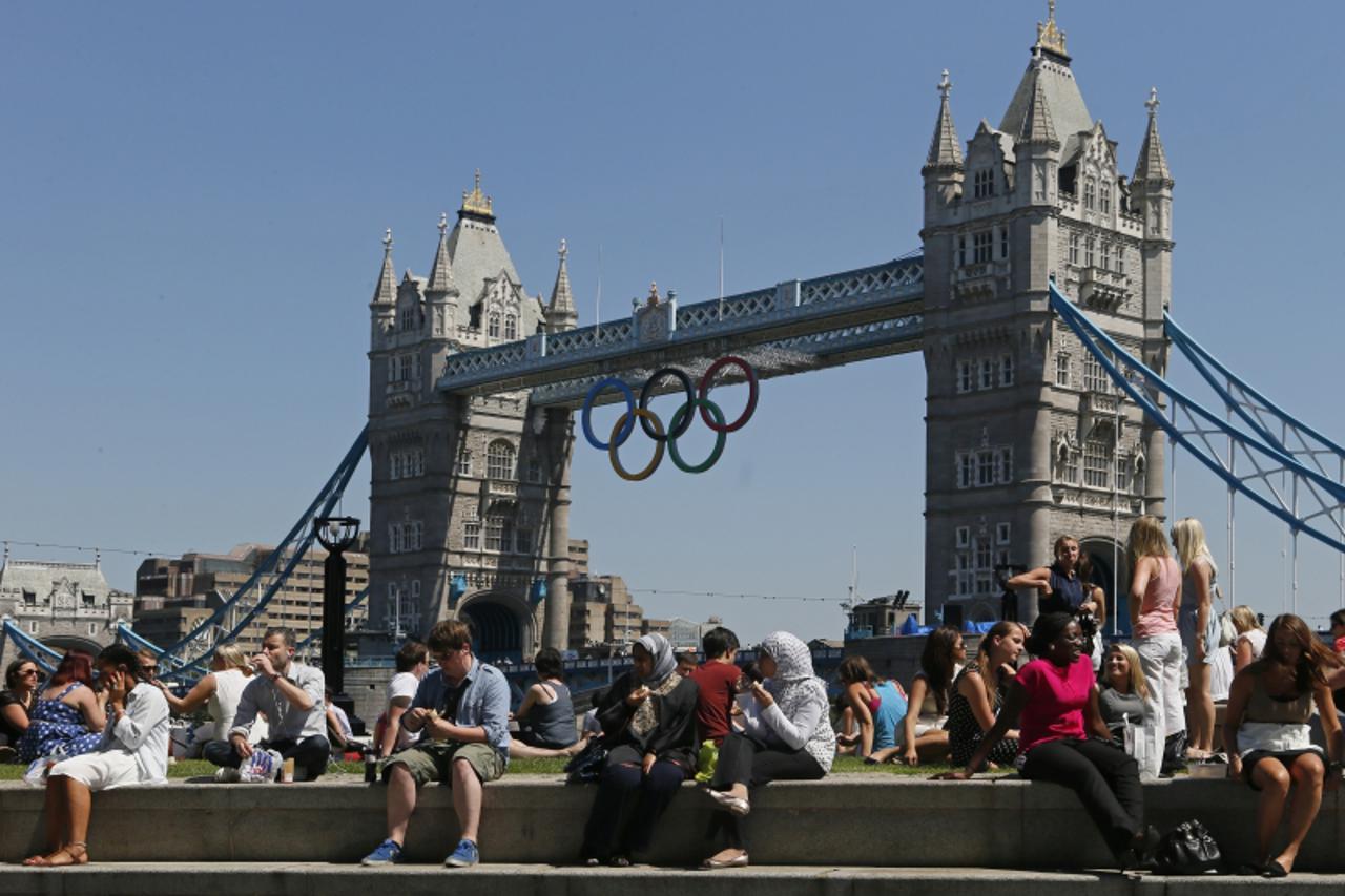 'epa03316460 People rest in front of the Tower Bridge decorated in Olympic rings in London, Britain, 24 July 2012. The London 2012 Olympic Games will start on 27 July.  EPA/SERGEI ILNITSKY'