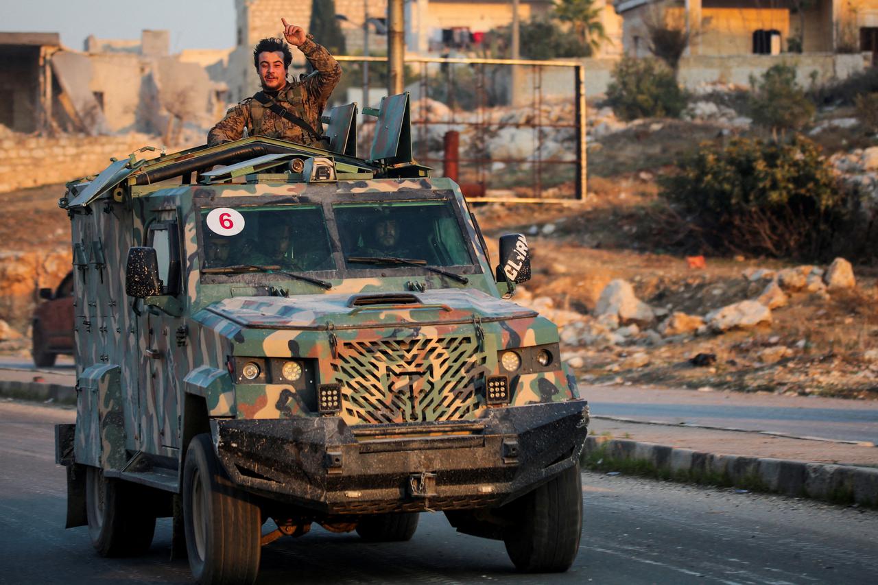 A rebel led by the Islamist militant group Hayat Tahrir al-Sham stands in the back of a vehicle in al-Rashideen