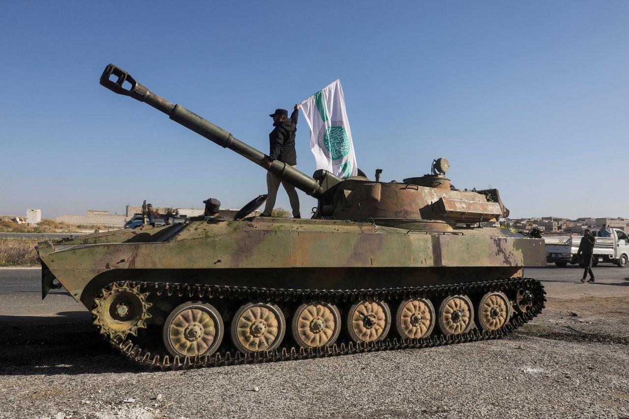 FILE PHOTO: A rebel fighter stands atop a military vehicle as he carries a Hayat Tahrir al-Sham flag in Saraqeb