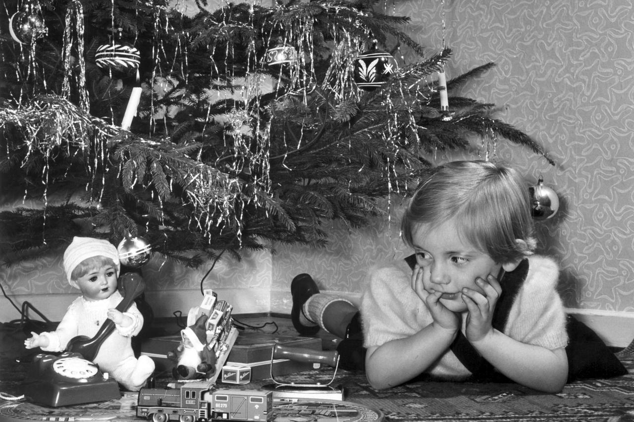 A small girl lies unter the Christmas tree on Christmas Eve 1955 and watches the presents, a doll, a children's phone and a model train.  Foto: Otto Noecker +++(c) dpa - Report+++/DPA/PIXSELL