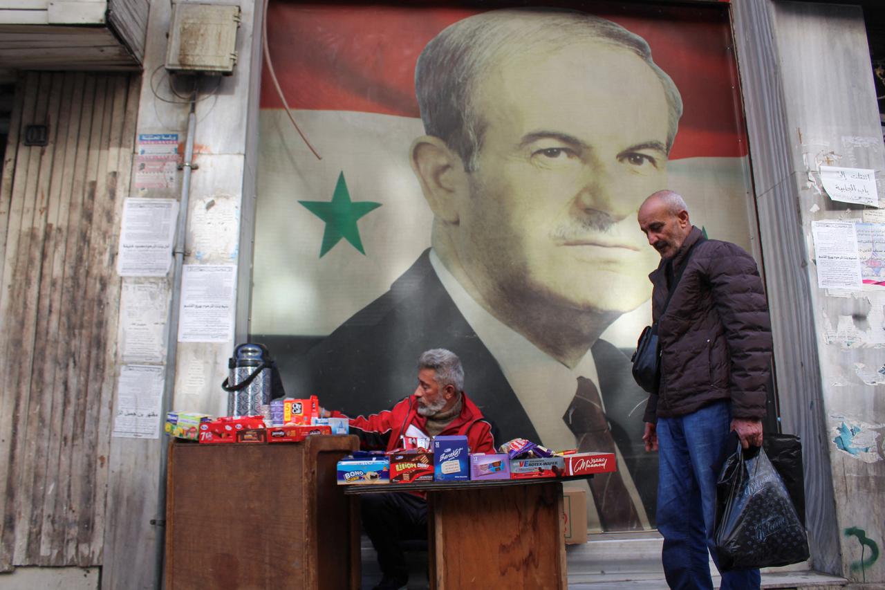 A street vendor sells sweets near a picture depicting former Syrian president Hafez al-Assad in Damascus