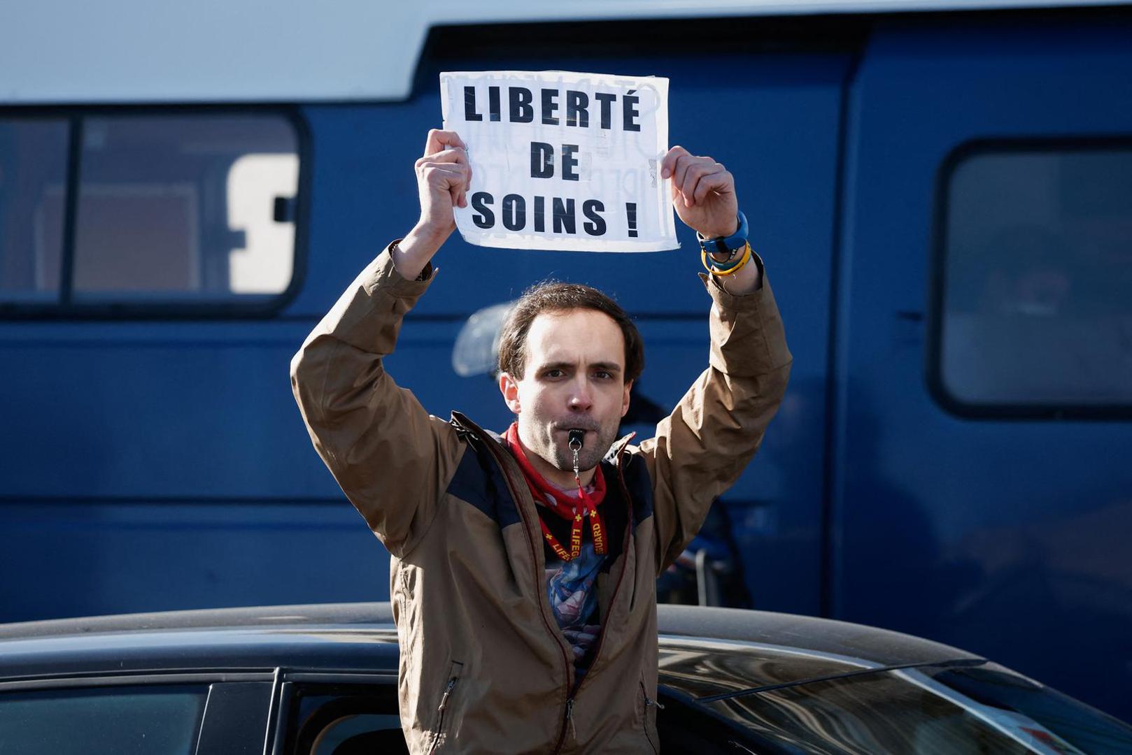 A demonstrator holds a sign reading "Freedom of care" on the Champs-Elysees avenue as cars parade during their "Convoi de la liberte" (The Freedom Convoy), a vehicular convoy to protest coronavirus disease (COVID-19) vaccine and restrictions in Paris, France, February 12, 2022. REUTERS/Benoit Tessier Photo: BENOIT TESSIER/REUTERS