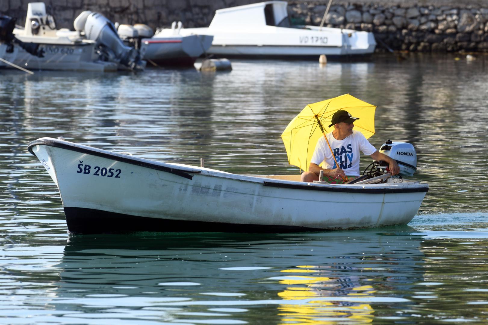 23.07.2022., Raslina - Spas od paklenih vrucina i jakoga sunca ovaj je mjestanin Rasline rijesio sa zutim kisobranom.
  Photo: Hrvoje Jelavic/PIXSELL