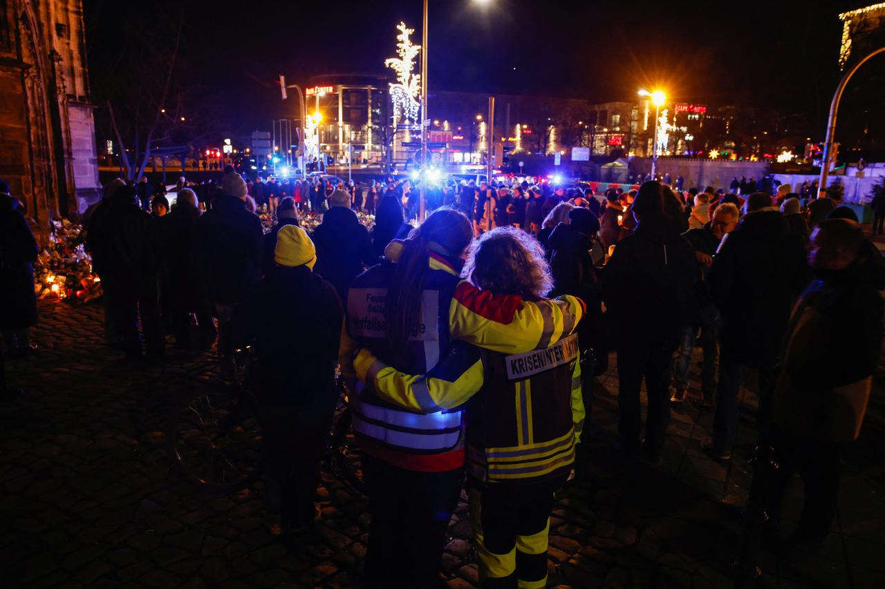 People stand near flowers and candles left as a tribute for the victims of the 'Alter Markt' Christmas market, in Magdeburg