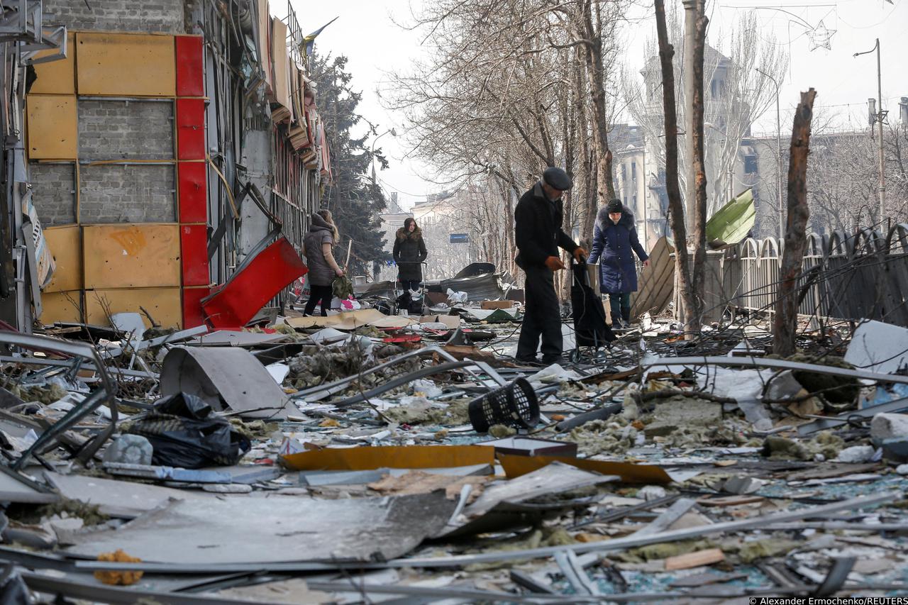 FILE PHOTO: Residents walk along a street near a building destroyed in the course of the Ukraine-Russia conflict, in Mariupol