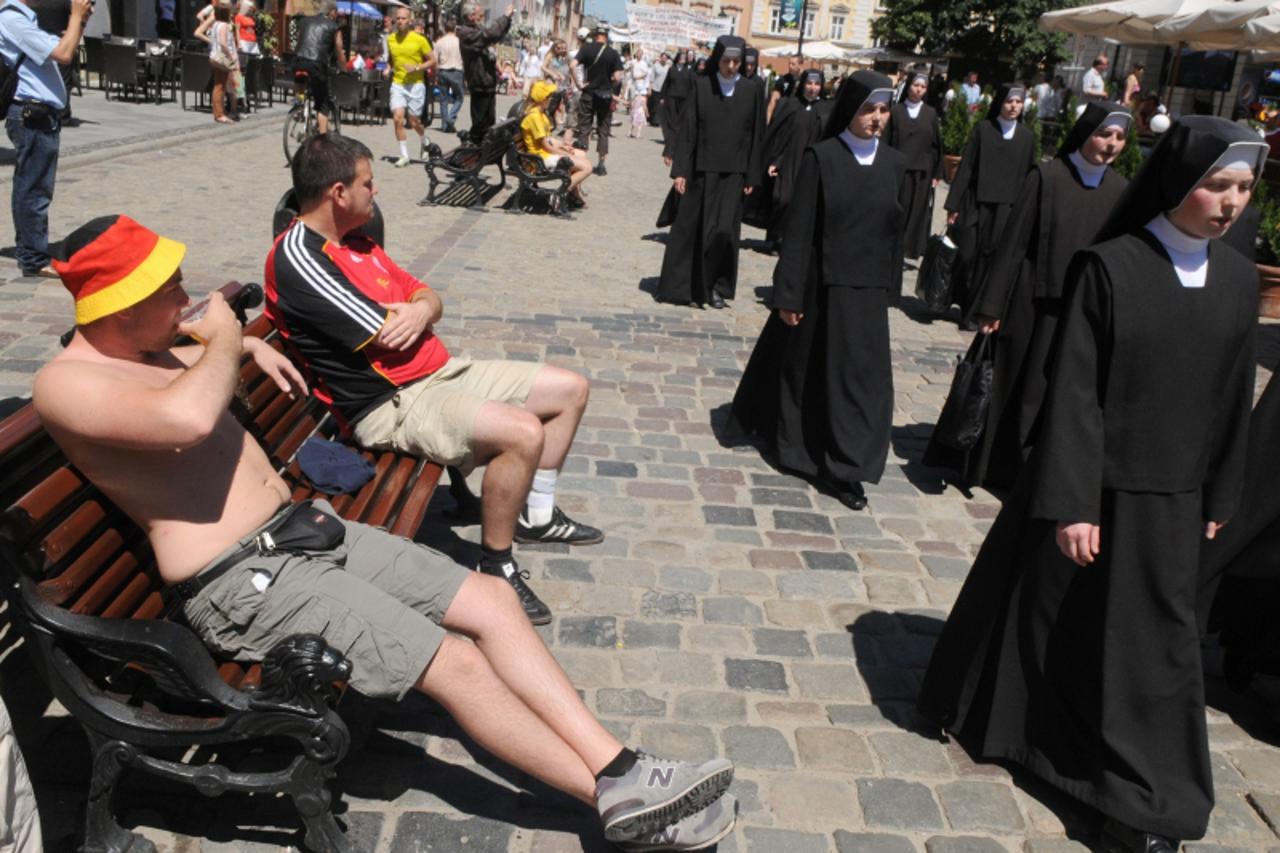 'German fans relax in the sunshine as they watch a procession of nuns pass by in Lviv\'s main square prior to the Group B clash Germany vs Denmark at the Euro 2012 football championships on June 17, 2