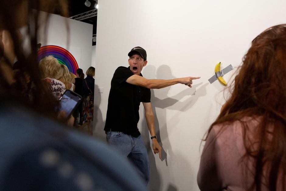 FILE PHOTO: A man poses for a photo next to a banana attached with duct-tape that replaces the artwork 'Comedian' by the artist Maurizio Cattelan, which was eaten by David Datuna, in Miami Beach