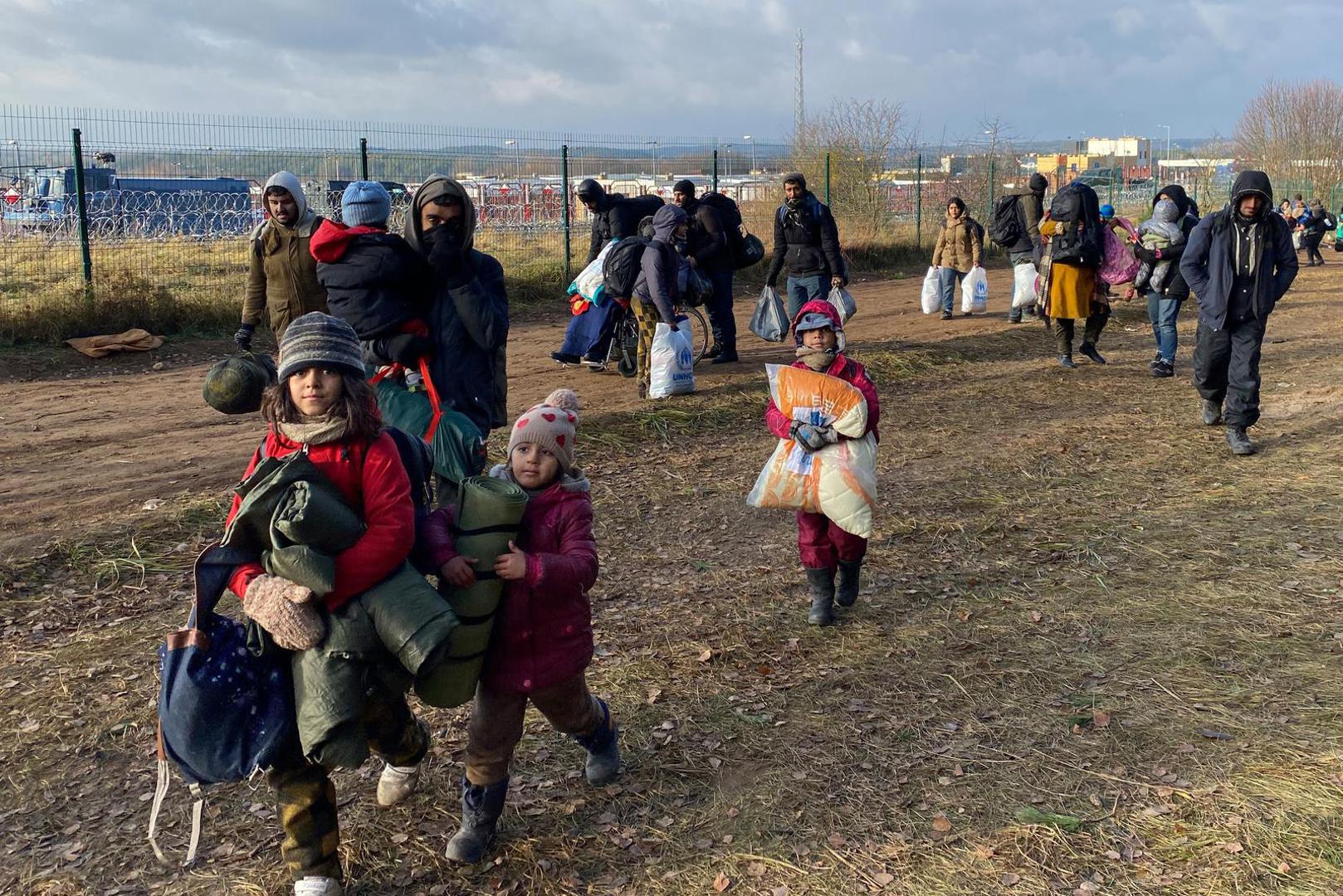 18 November 2021, Belarus, Brusgi: Migrants walk with their luggage in front of the border in Belarus at the closed crossing with Poland. More and more migrants are packing their bags to move to emergency accommodation. Thousands of migrants have been holding out for days at the Belarusian-Polish border. Photo: Ulf Mauder/dpa