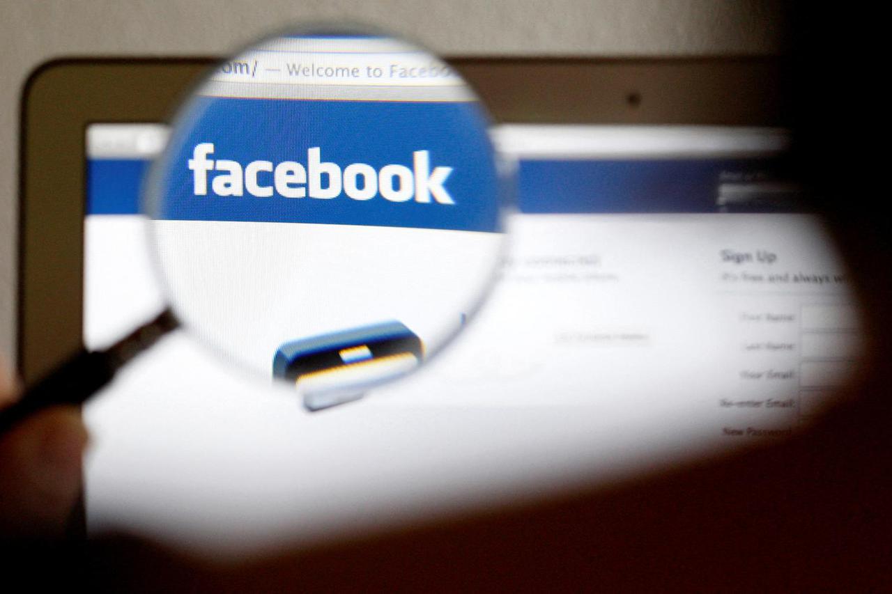 FILE PHOTO: In this photo illustration, a Facebook logo on a computer screen is seen through a magnifying glass held by a woman in Bern