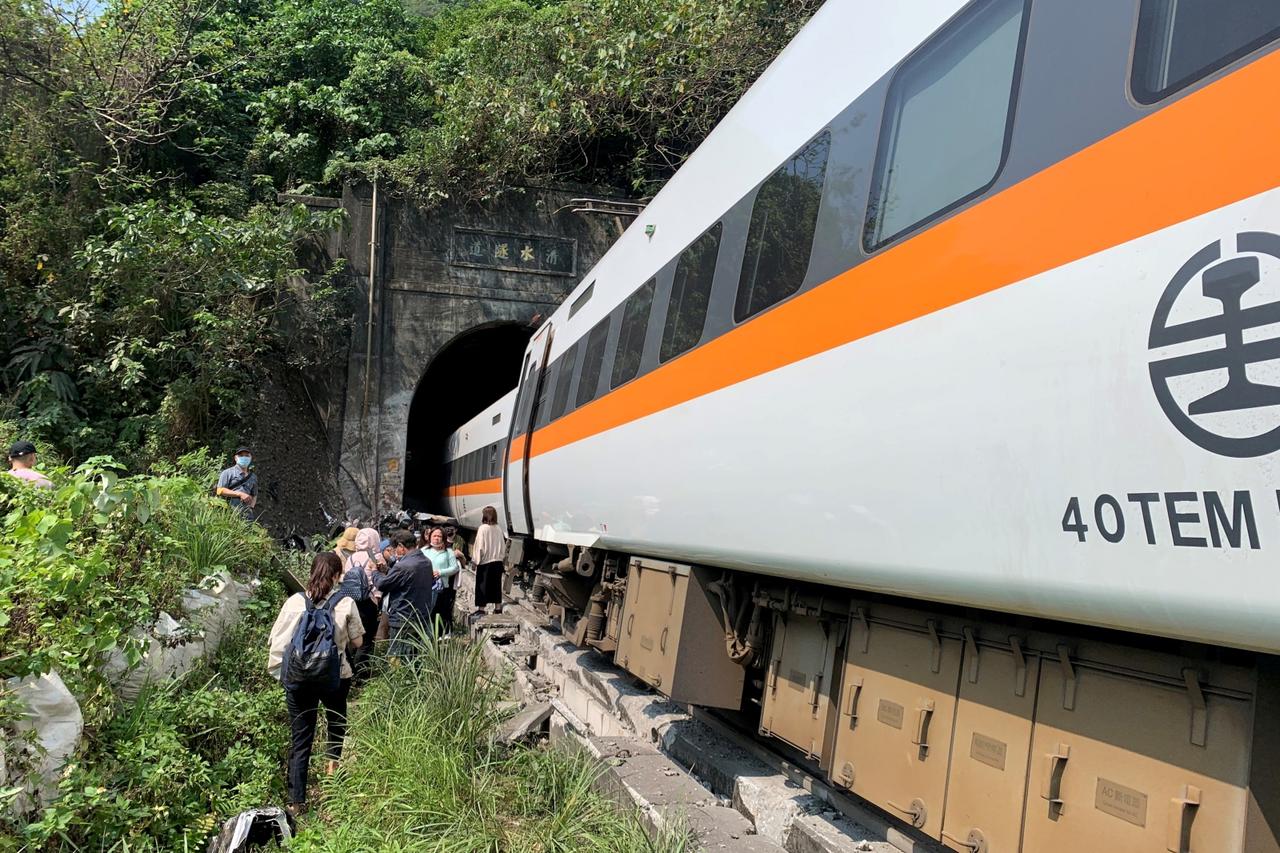 People walk next to a train which derailed in a tunnel north of Hualien