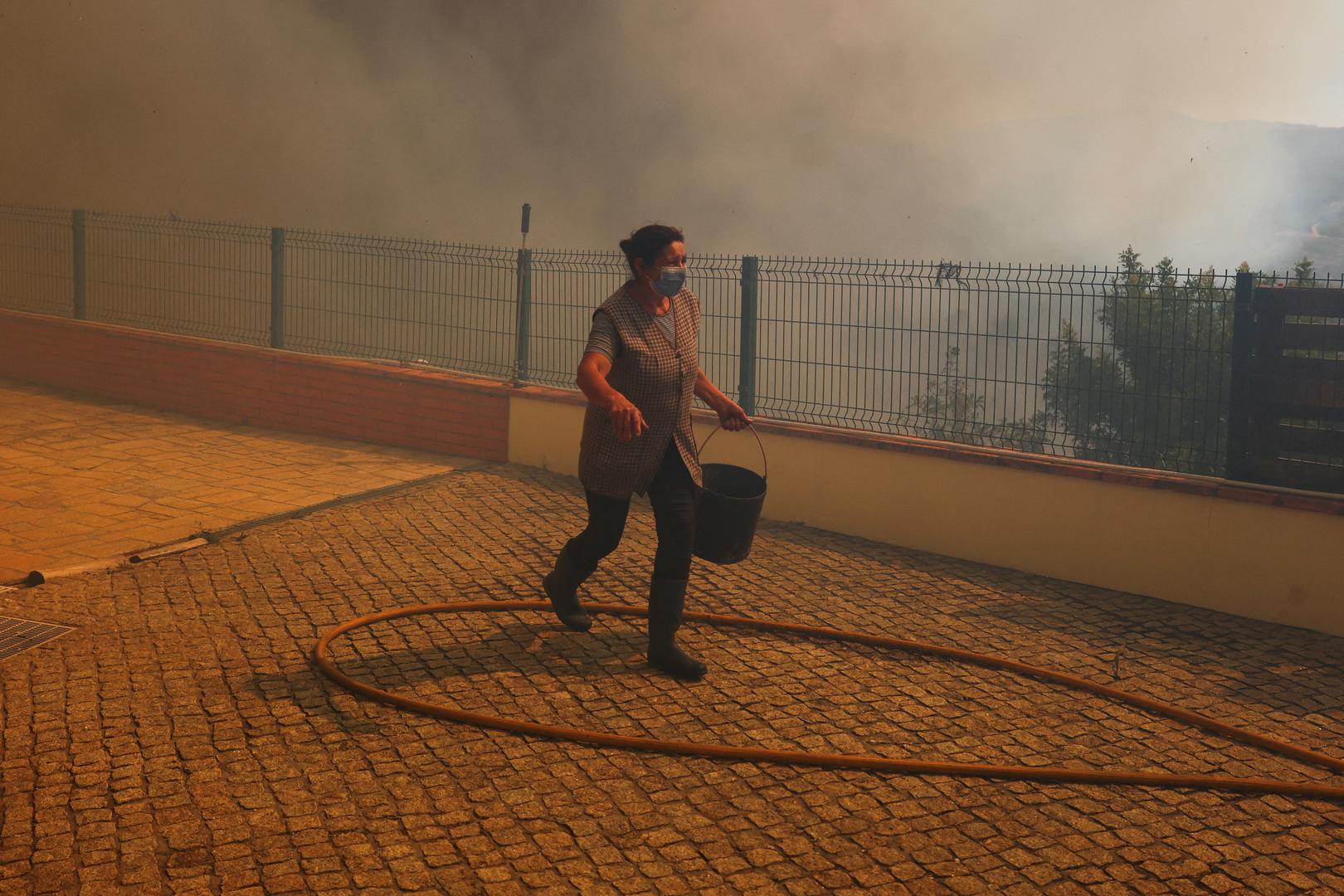 A woman walks with a bucket of water during a wildfire in Vilarinho, Portugal, September 17, 2024. REUTERS/Pedro Nunes Photo: PEDRO NUNES/REUTERS