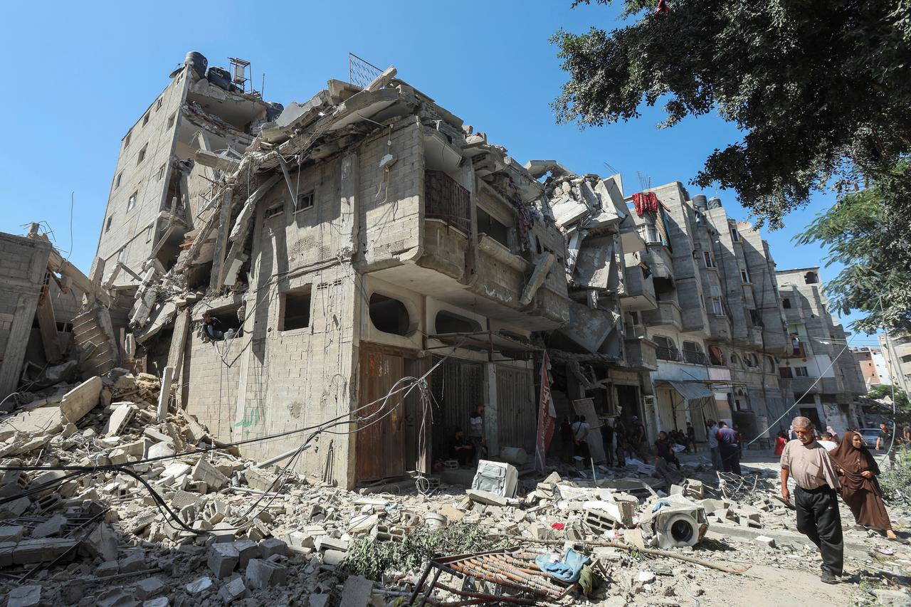 Palestinians walk past a house hit in an Israeli strike, amid the Israel-Hamas conflict, in Bureij refugee camp, in the central Gaza Strip