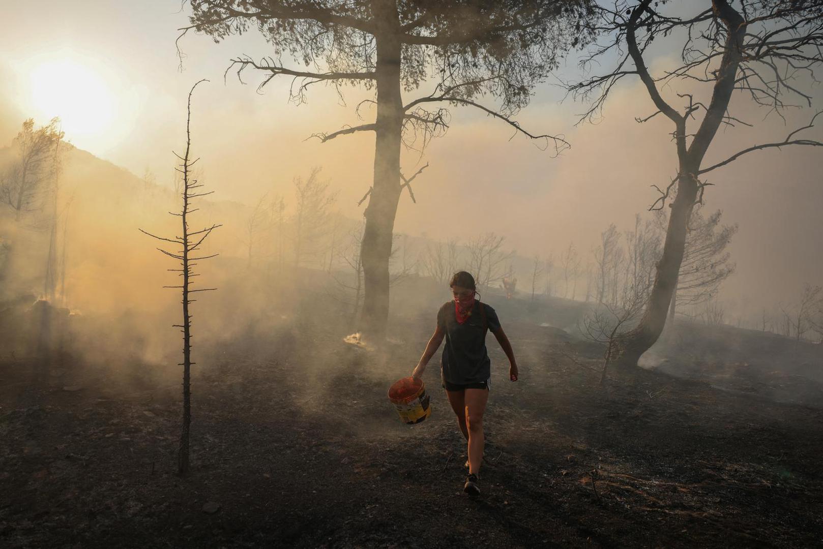 Marina Kalogerakou, 24, carries a bucket, as a wildfire burns in Penteli, Greece, August 12, 2024. REUTERS/Stelios Misinas Photo: STELIOS MISINAS/REUTERS