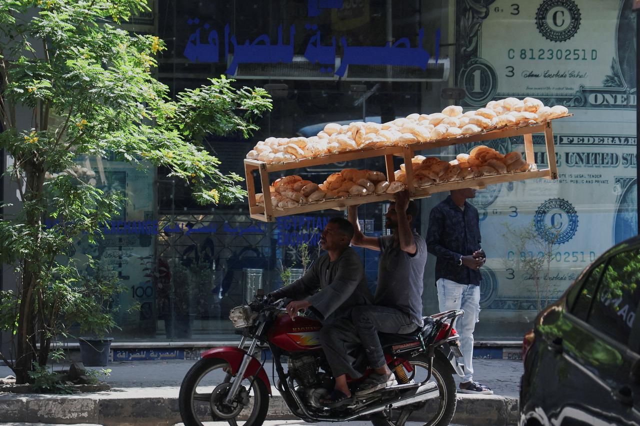 FILE PHOTO: Egyptian street vendors carrying breads, drive past a currency exchange point, displaying images of the U.S. dollar, in Cairo