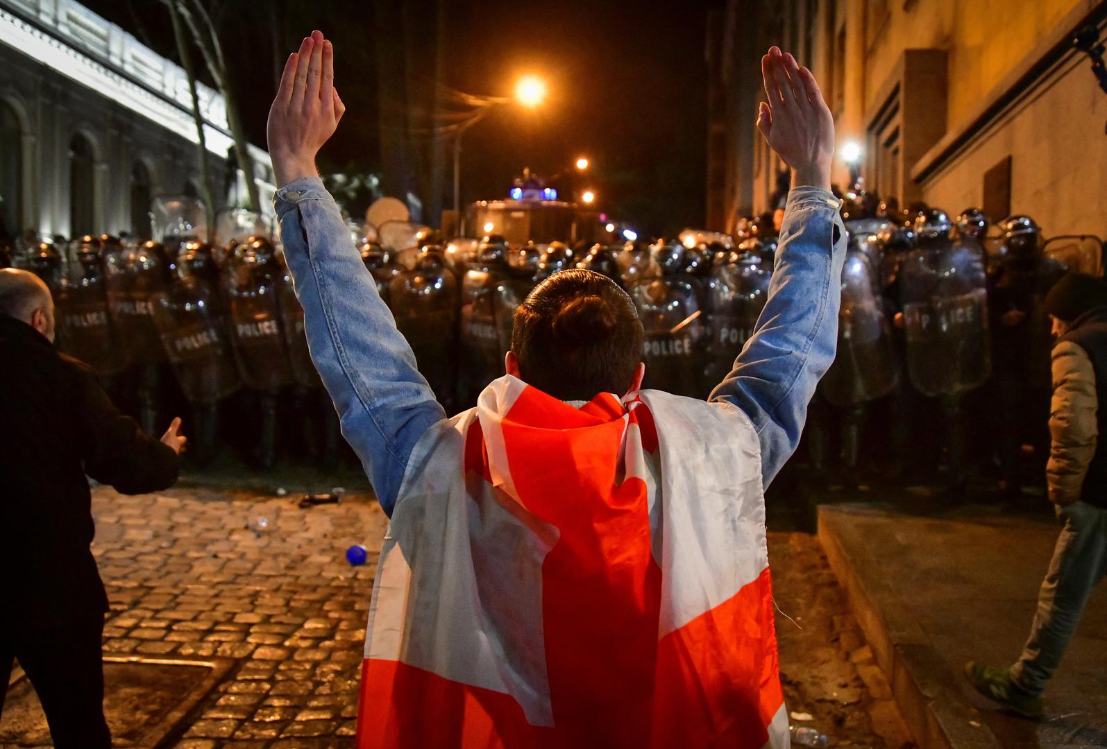 A protester wrapped in a Georgian national flag raises hands while standing in front of law enforcement officers during a rally against the "foreign agents" law in Tbilisi, Georgia, March 7, 2023. REUTERS/Zurab Javakhadze Photo: ZURAB JAVAKHADZE/REUTERS