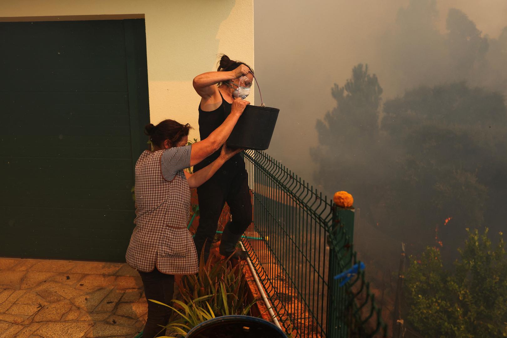 Two women carry a bucket of water as the wildfire approaches their house in Vilarinho, Portugal, September 17, 2024. REUTERS/Pedro Nunes Photo: PEDRO NUNES/REUTERS