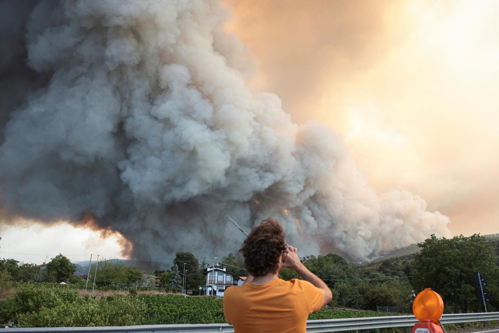 A person records as smoke billows from a wildfire over the border with Slovenia seen from Rupa, Italy, July 20, 2022. REUTERS/Borut Zivulovic Photo: BORUT ZIVULOVIC/REUTERS