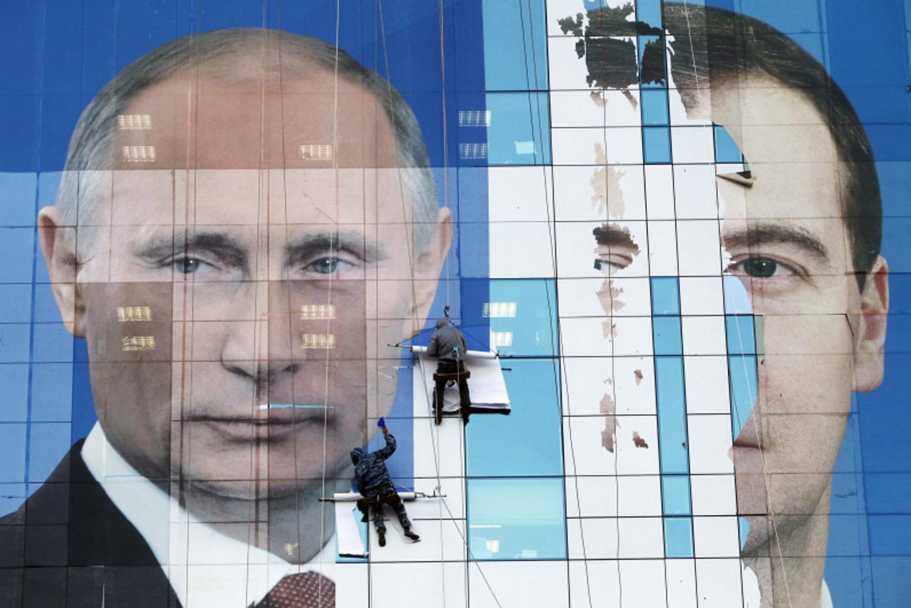 'Workers attach a pre-election poster featuring Russia\'s President Dmitry Medvedev (R) and Prime Minister Vladimir Putin, appealing to people to vote for the United Russia political party, onto an of