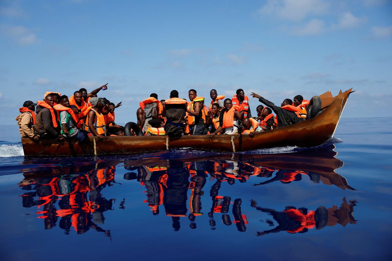 Migrants sail on an iron boat near NGO Open Arms rescue boat