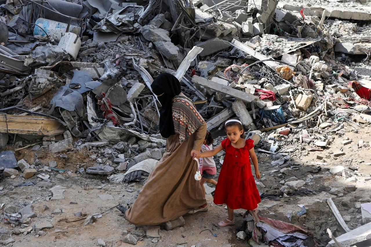 A woman and child walk among debris, aftermath of Israeli strikes at the area, where Israeli hostages were rescued on Saturday, as Palestinian death toll rises to 274, amid the Israel-Hamas conflict, in Nuseirat refugee camp in the central Gaza Strip