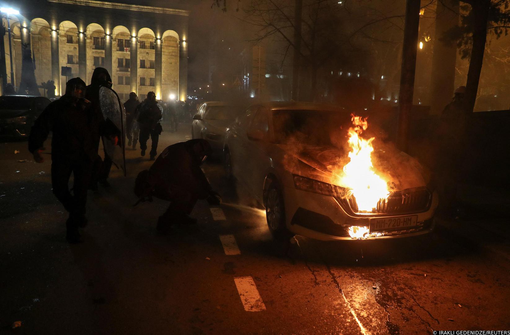 Law enforcement officers approach a car to put out a fire during a rally against the "foreign agents" law near the parliament building Tbilisi, Georgia, March 8, 2023. REUTERS/Irakli Gedenidze Photo: IRAKLI GEDENIDZE/REUTERS