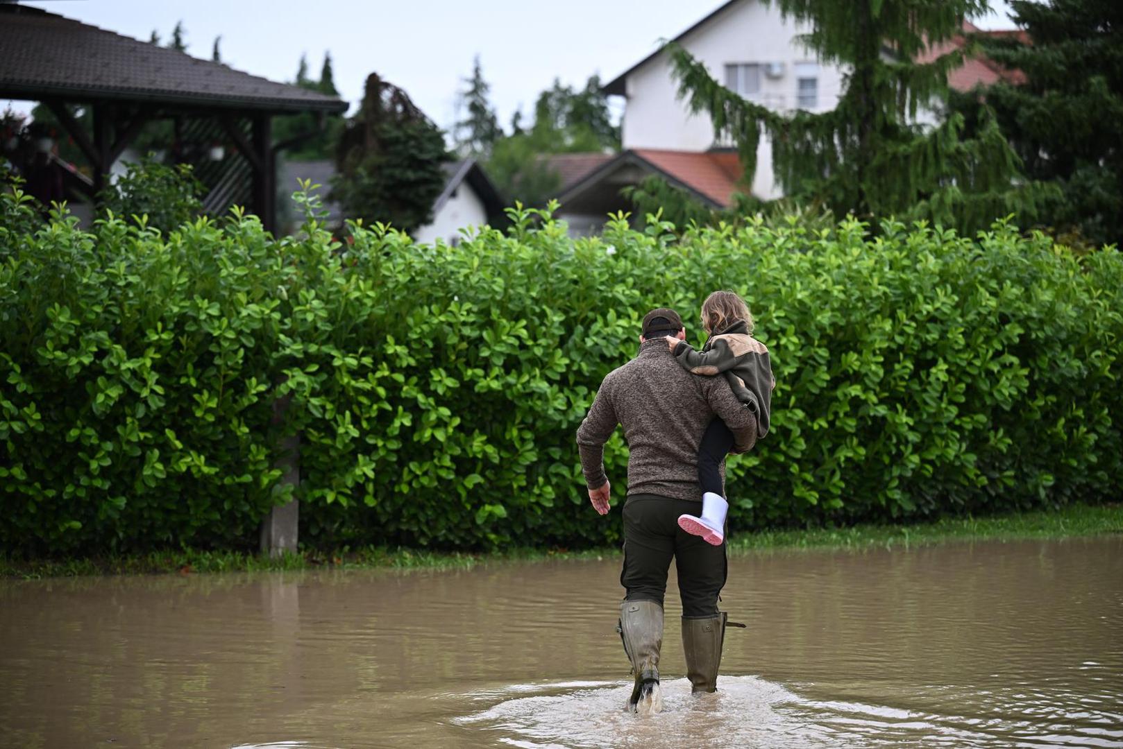 05.08.2023., Drenje Brdovecko - Zbog izlijevanja rijeke Save, voda prijeti kucama u Drenju Brdoveckom. Covjek nosi kcerku preko poplavljene prometnice. Photo: Davor Puklavec/PIXSELL