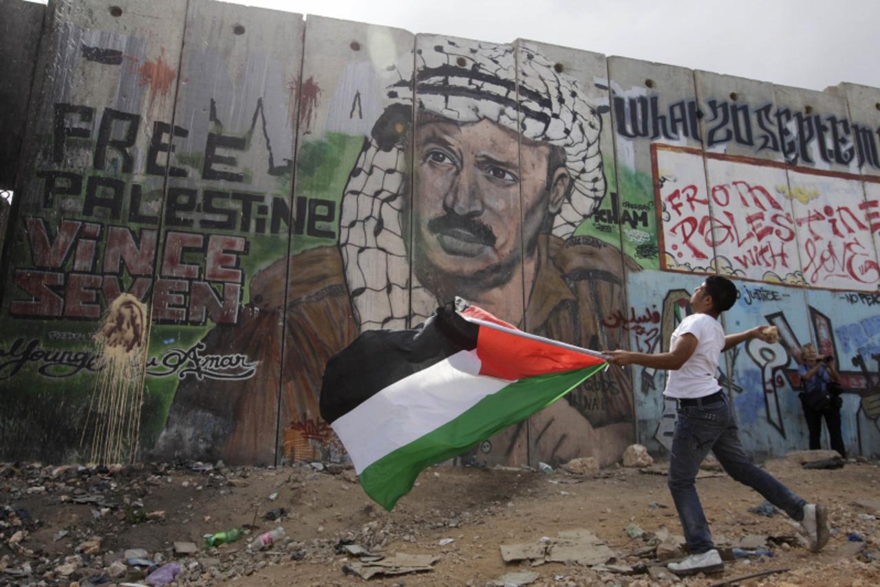 \'A Palestinian youth holds a flag as he throws a stone in front of a mural depicting the late Palestinian leader Yasser Arafat on the controversial Israeli barrier, during clashes with Israeli troops