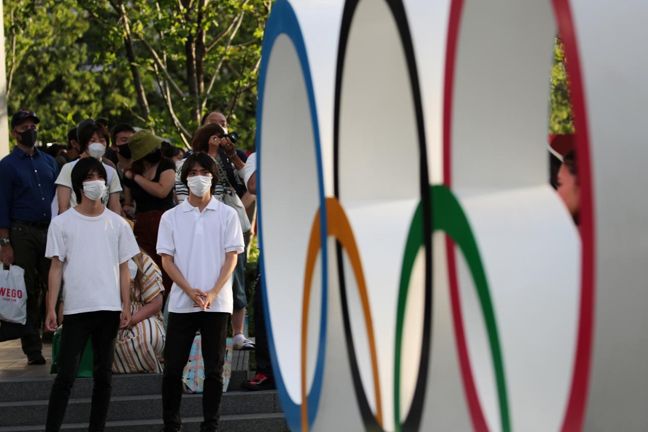 People wearing protective masks stand in front of the Olympic Ring near the National Stadium, in Tokyo