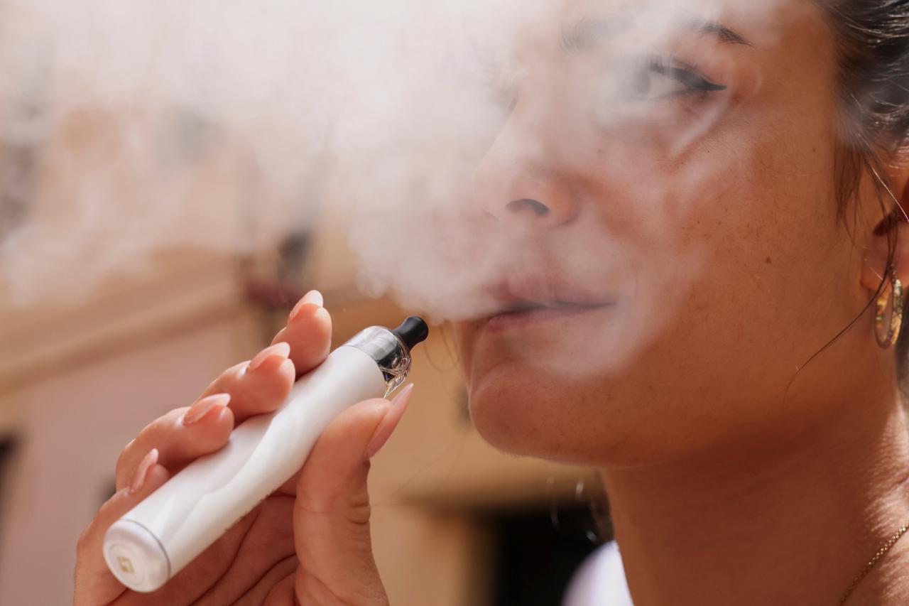 A woman smokes an e-cigarette in the public space