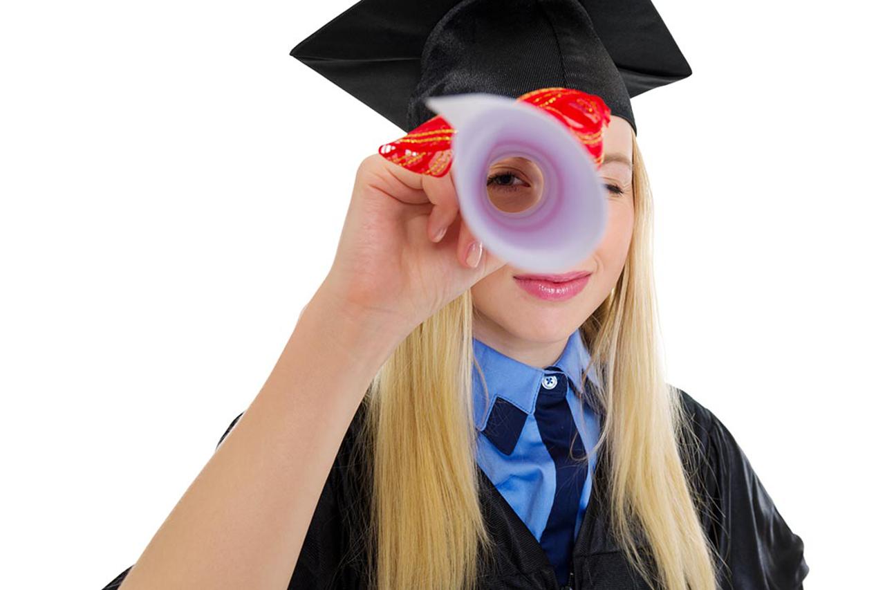 Young woman in graduation gown looking through diploma